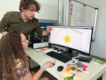 Construction Electrician 2nd Class Rachelle McIntyre assigned to Public Works Department Souda Bay, Greece gets assistance on prepping for a 3D print job during a Community Relations project April 20, 2024. This COMREL empowered Seabees to practice 3D printing methods at the Transformable Intelligent Environments Lab at the School of Architecture and Engineering, Technical University of Crete, Greece, interact with the participants, and gain insight into the transformative potential of this technology. NSA Souda Bay is an operational ashore installation which enables and supports U.S., Allied, Coalition, and Partner nation forces to preserve security and stability in the European, African, and Central Command areas of responsibility. (U.S. Navy photo by Nicholas S. Tenorio)
