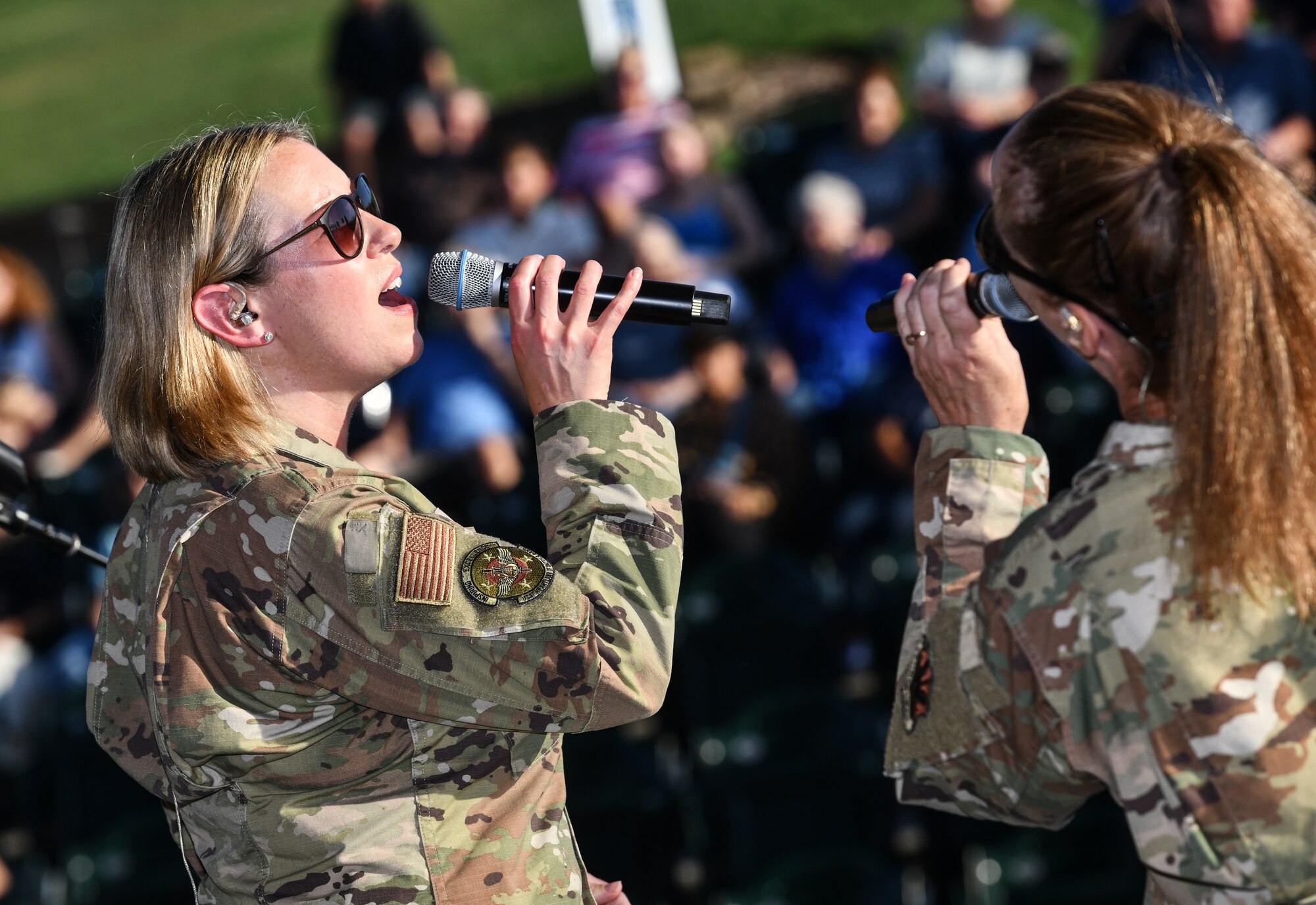 two female singers in military uniform sing in front of a crowd
