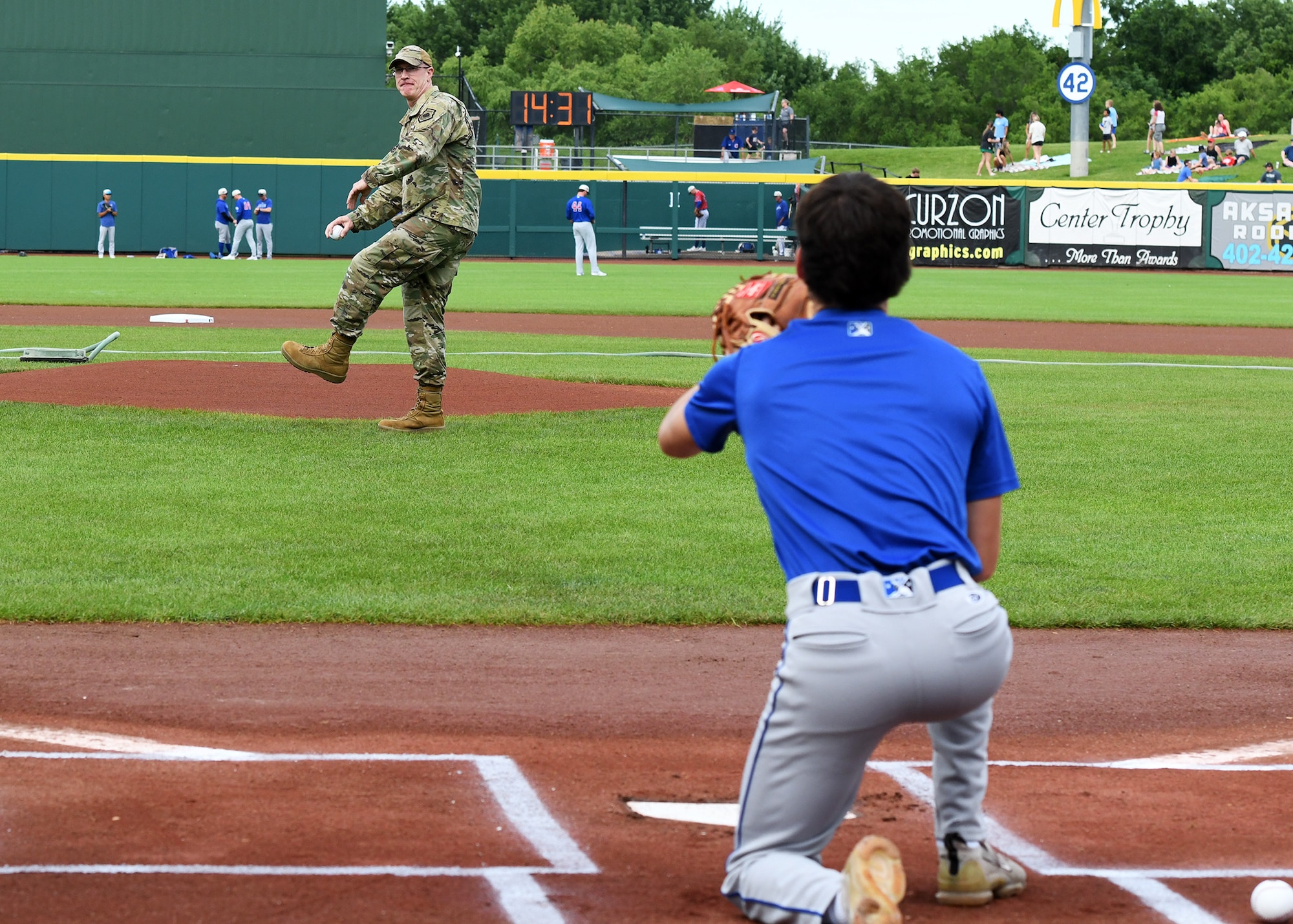 Man in military uniform throws a pitch at a catcher in baseball uniform