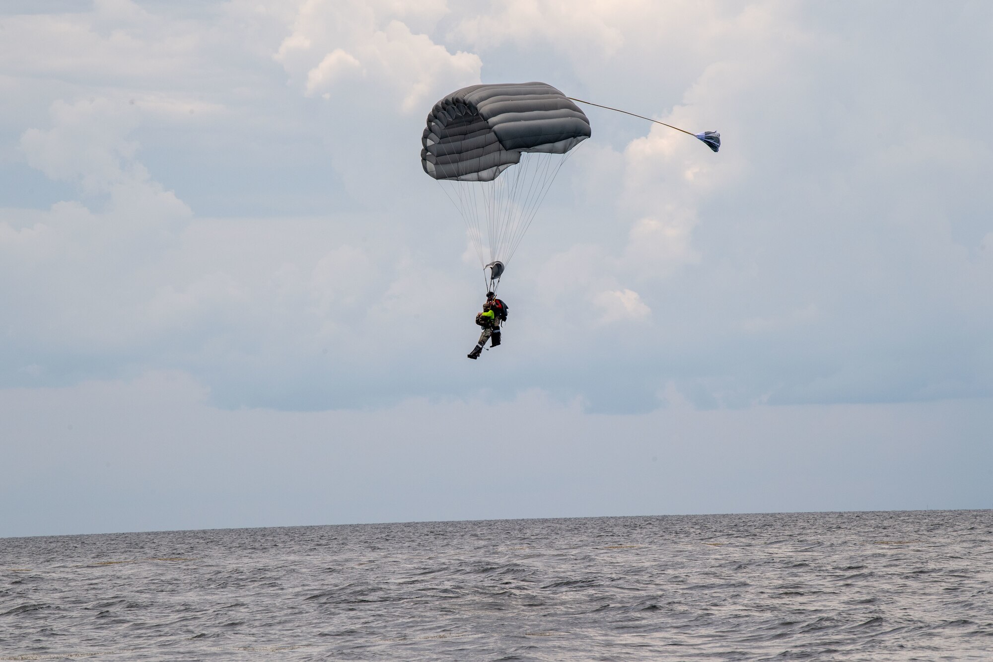 U.S. Air Force Chief Master Sgt. Justin Geers, 23rd Wing command chief, prepares for landing after jumping tandem with a pararescueman from the 38th Rescue Squadron during a battlefield circulation in the Gulf of Mexico, June 24, 2024. Pararescue jumpers parachute from airplanes to rescue and treat injured military personnel in austere locations. PJs are highly trained specialists skilled in parachuting, scuba diving, rock climbing and arctic survival. (U.S. Air Force photo by 2nd Lt. Benjamin Williams)