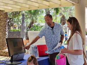 JOINT BASE PEARL HARBOR-HICKAM, Hawaii (July 3, 2024) A community liaison for Navy Closure Task Force-Red Hill (NCTF-RH) shows a resident testing results and shares information about the Extended Drinking Water Monitoring (EDWM) and Water Quality Action Team (WQAT) programs at the Hickam Exchange in Joint Base Pearl Harbor-Hickam (JBPHH), Hawaii, July 3, 2024. The Navy voluntarily instituted the EDWM and WQAT programs in April following the end of the two-year drinking water Long-Term Monitoring program. The programs are designed to provide resources and enhanced water sampling and testing for residents on the JBPHH water system. (U.S. Navy photo by Mass Communication Specialist Seaman Krystal Diaz)