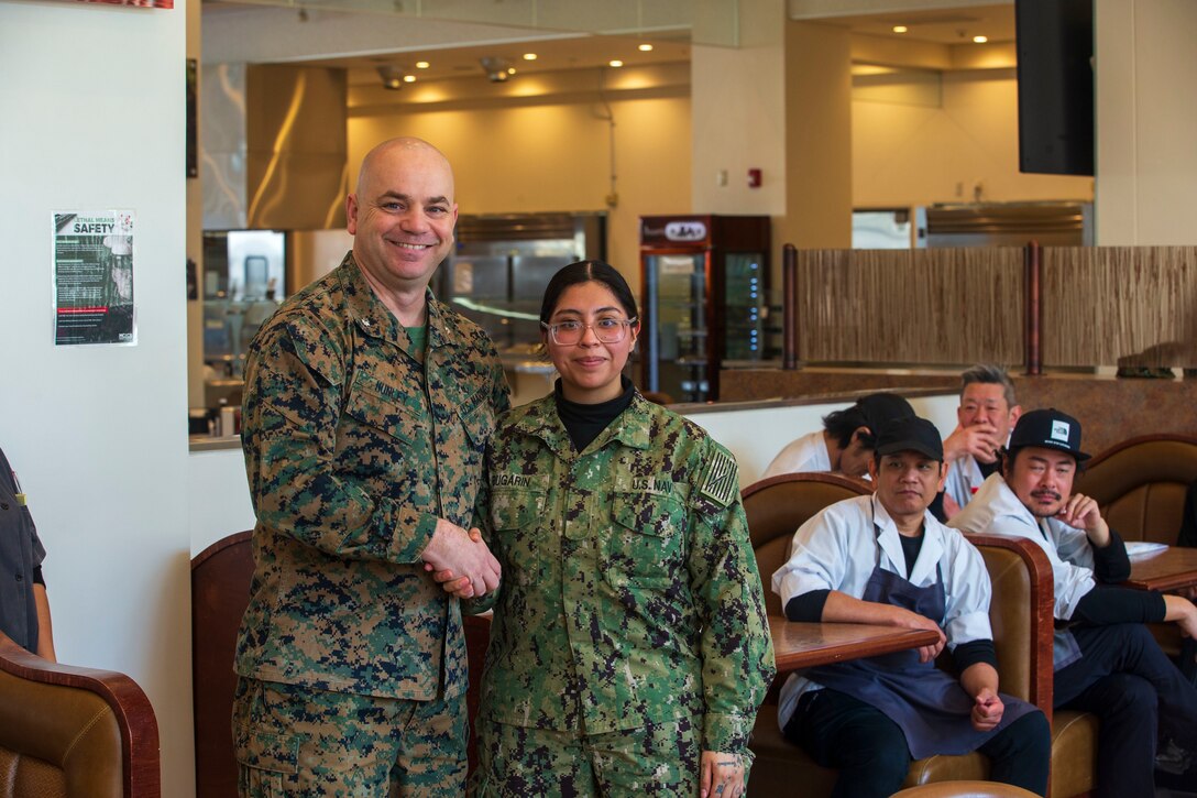 U.S. Marine Corps Lt. Col David Hunley, left, the director of food services for Marine Corps Installations Command, poses for a photo with U.S. Navy Commissaryman Seaman Recruit Leticia Bugarin with Headquarters and Headquarters Squadron, Marine Corps Air Station Iwakuni, after giving her a challenge coin for outstanding work while taking part in the Maj. Gen. William Pendleton Thompson (W.P.T.) Hill memorial awards program, at MCAS Iwakuni, Japan, Jan. 29, 2024. The W.P.T. Hill awards program aims to acknowledge outstanding performance within Marine Corps food service operations, including determining and recognizing the best mess halls of the year.