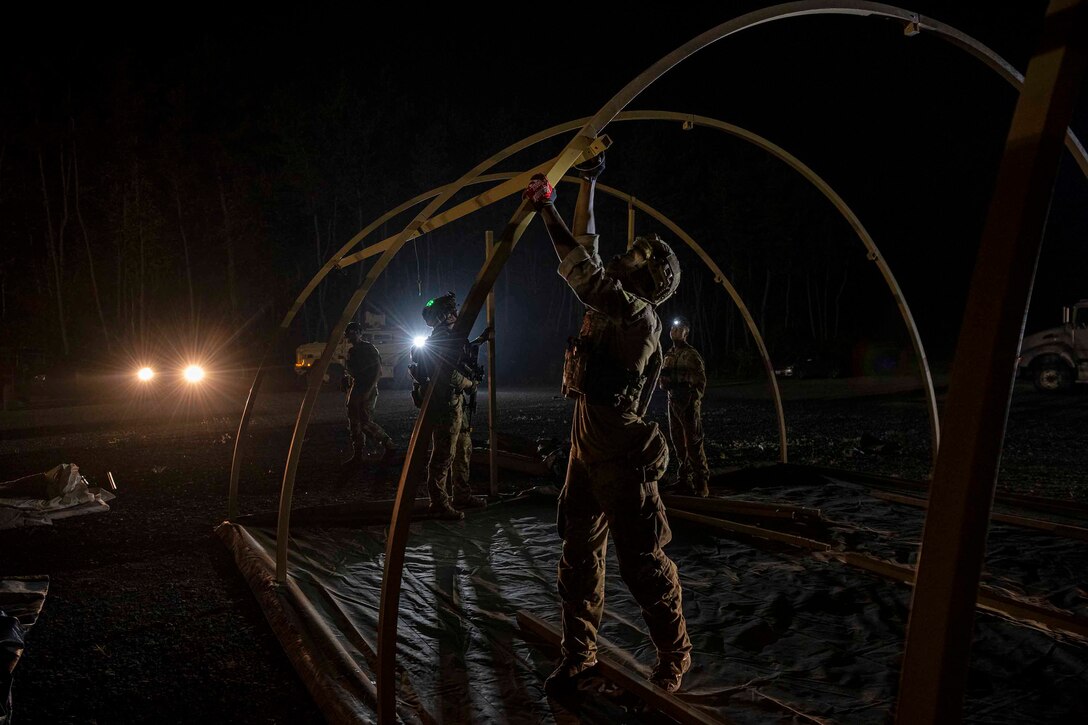 A group of airmen set up a large tent at night using the headlights of a vehicle to see.