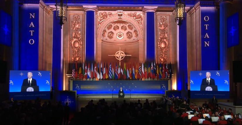 A man wearing a business suit stands at a lectern on a stage.