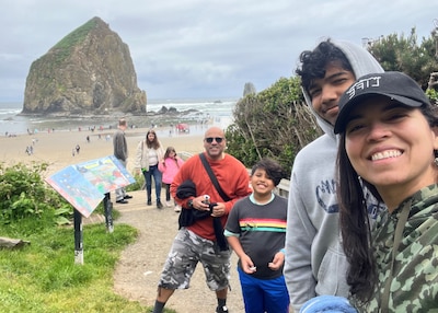 With a overcast sky a family of four Mon, two sons and dad look into the camera with the beach in the background on an overcast day.