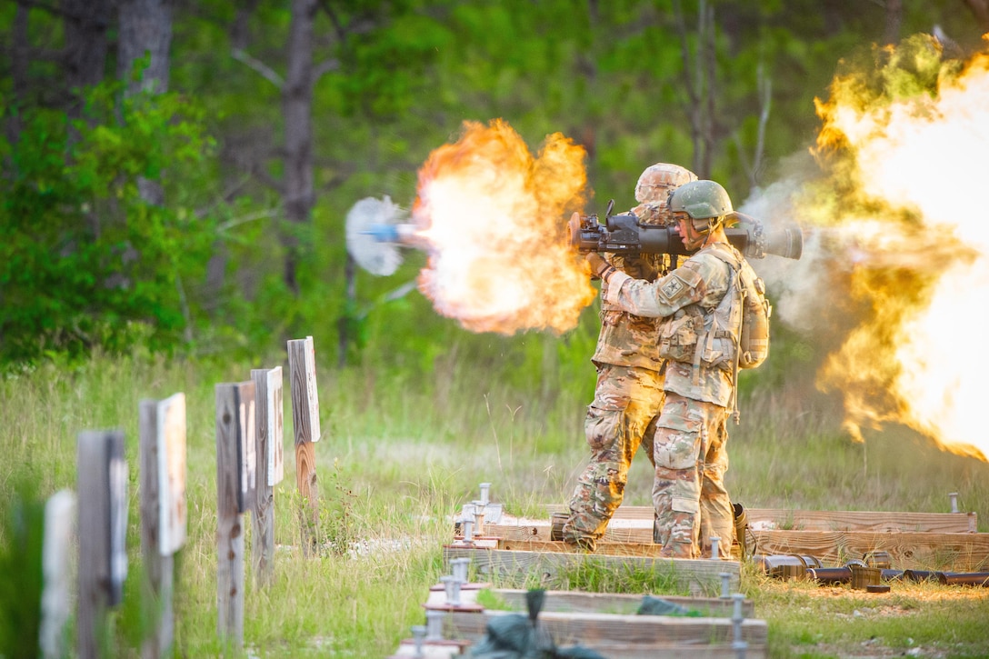 Two soldiers fire weapons in a field, creating fireballs.