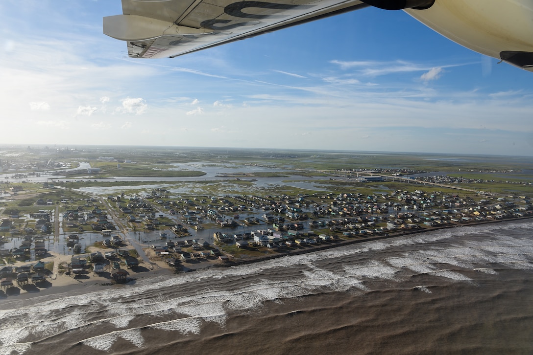 The wing of a Coast Guard aircraft can be seen in a daylight aerial view of a partially flooded shoreline community.