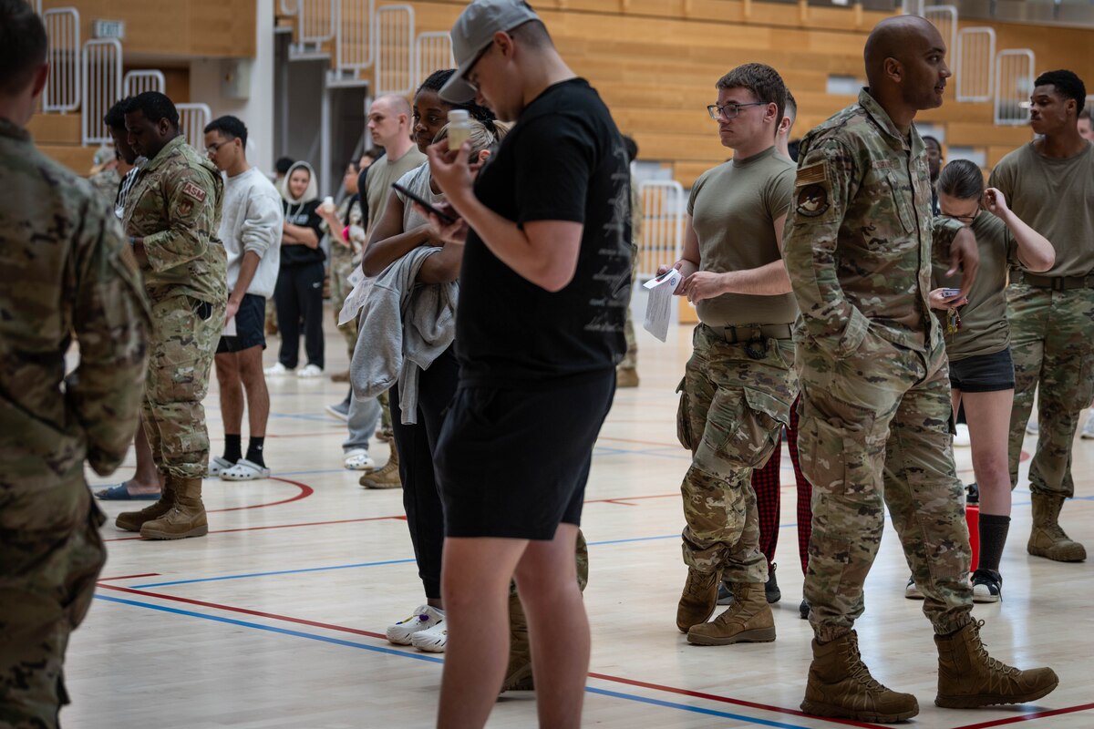 Airmen wait in line with urine samples in a gym.