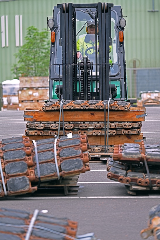 A man in a forktruck moves stacks of tank treads.