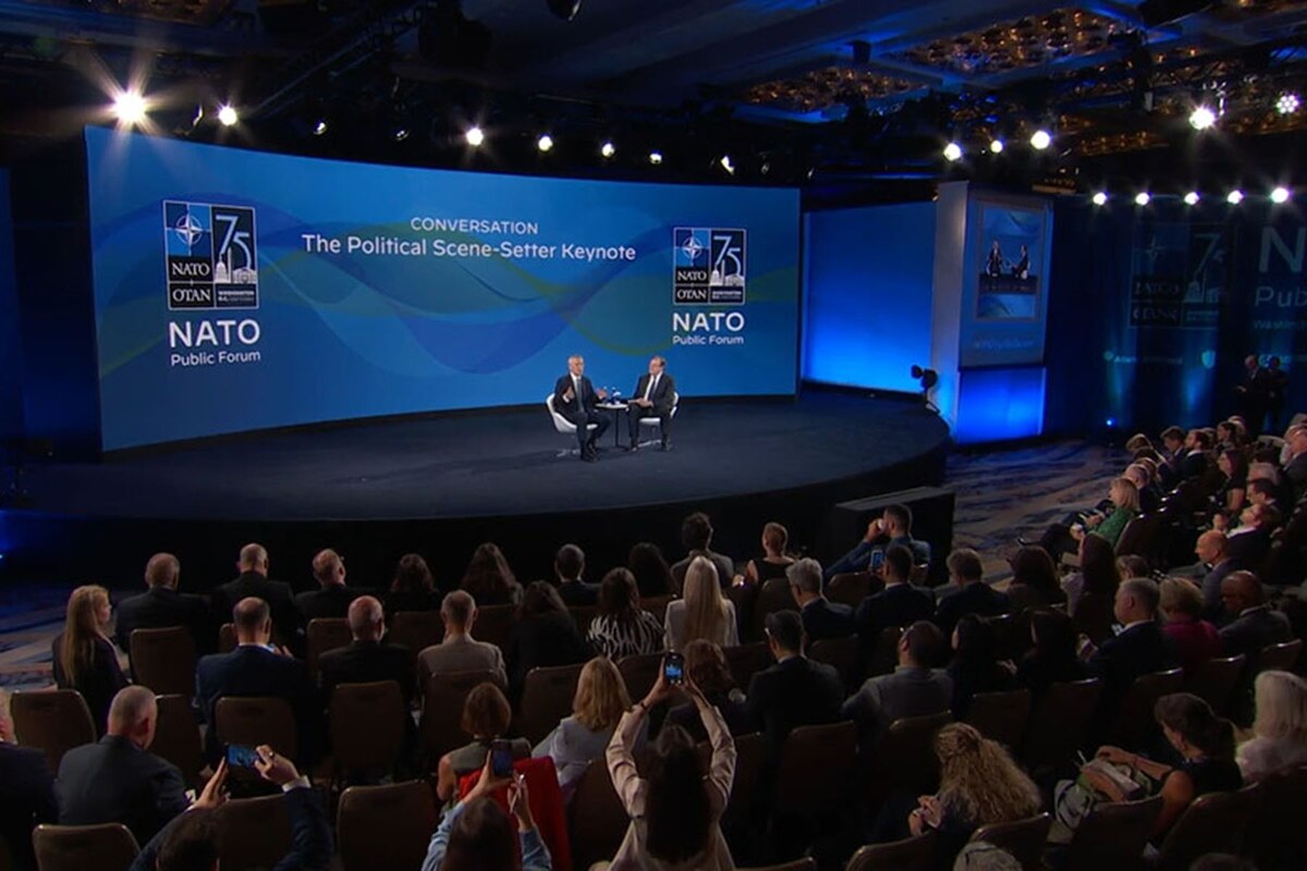Two people sit on a stage in front of an audience.