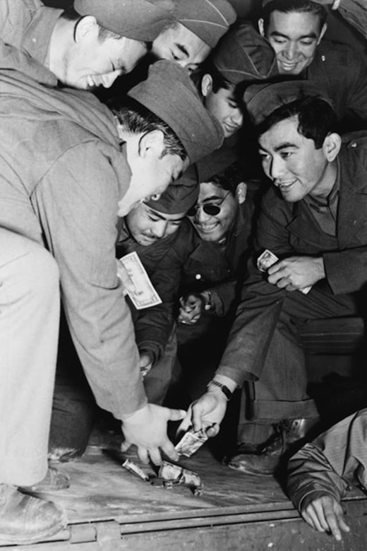 Service members seated in a circle reach toward the ground with money.