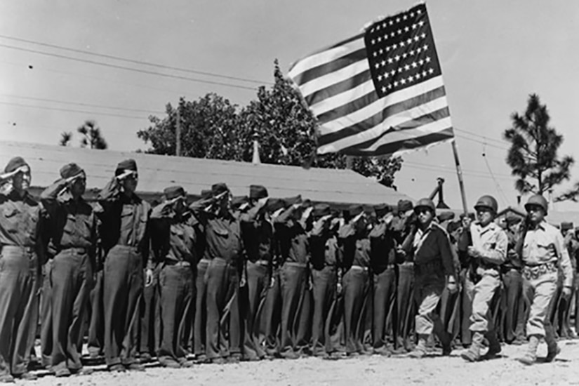 Service members stand at attention as a person carrying the U.S. flag walks past.