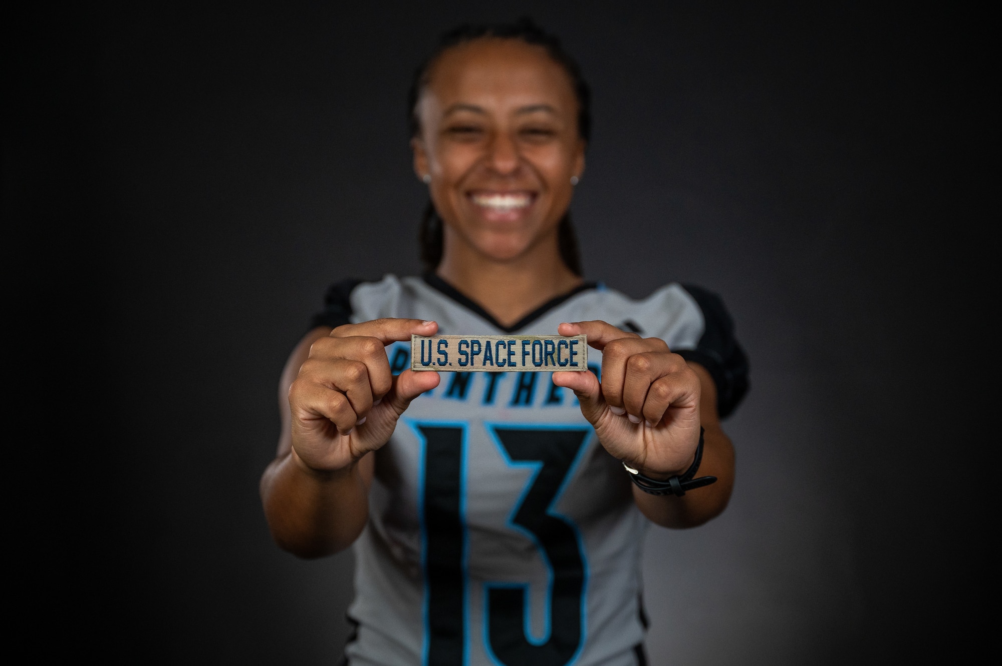 A woman in a football jersey holds a U.S. Space Force name tape towards the camera.