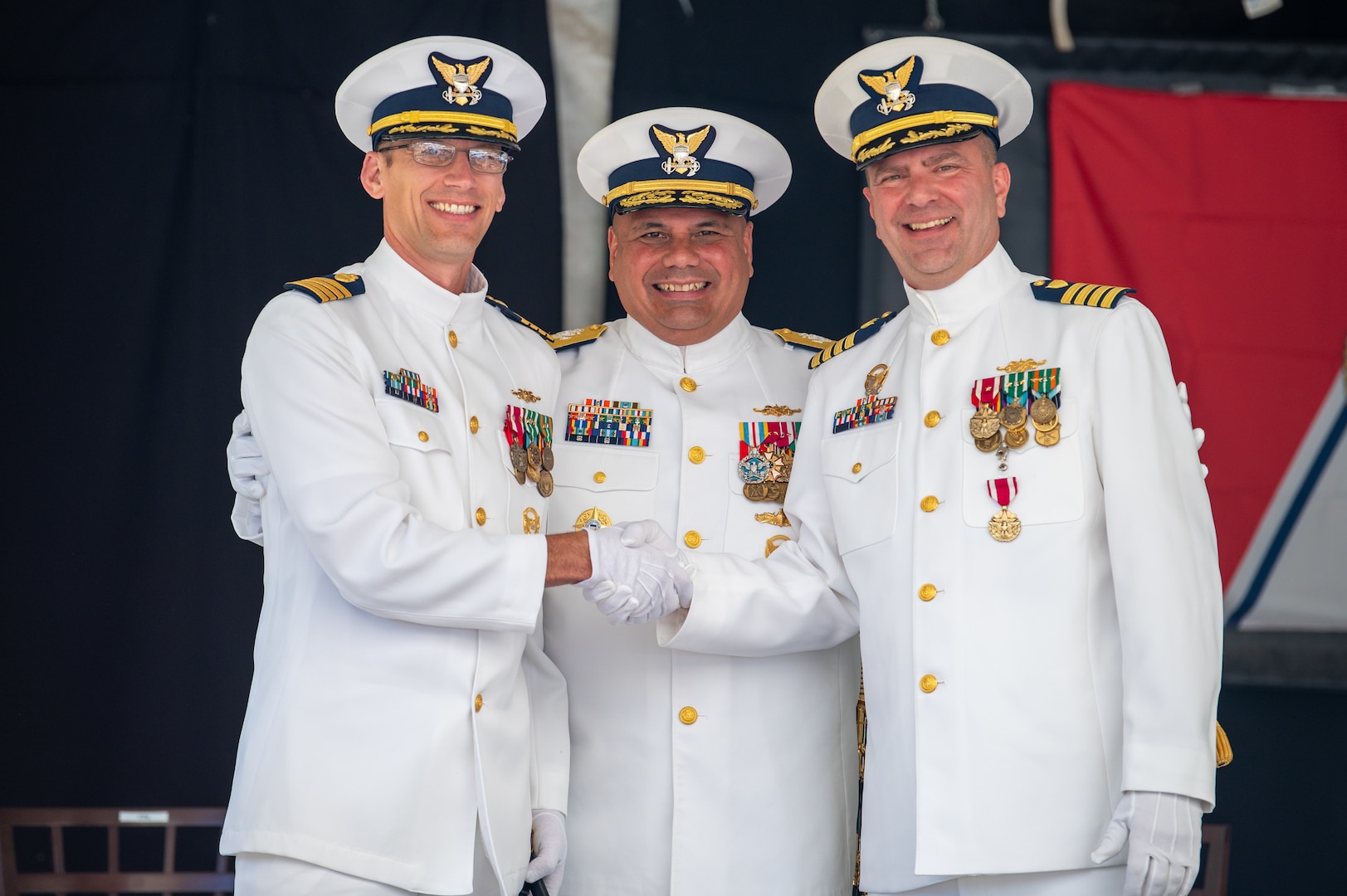 U.S. Coast Guard Capt. Jeffrey Rasnake shakes hands with Capt. Keith Ropella with Vice Adm. Andrew Tiongson standing between them.