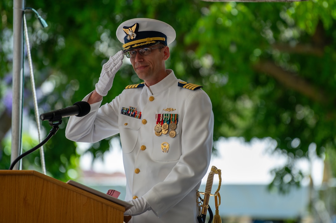 U.S. Coast Guard Capt. Jeffrey Rasnake stands behind a podium and salutes to the crew of the Coast Guard Cutter Polar Star (not seen in image?