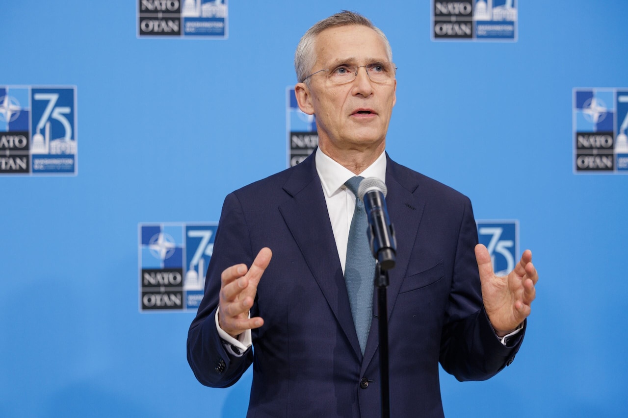 A man in business attire gestures with his hands while standing at a microphone.
