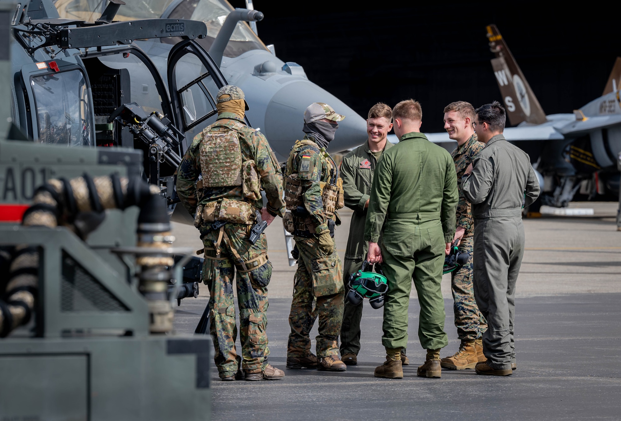 A group of 6 U.S., and German service members  stand together and talk in a circle.
