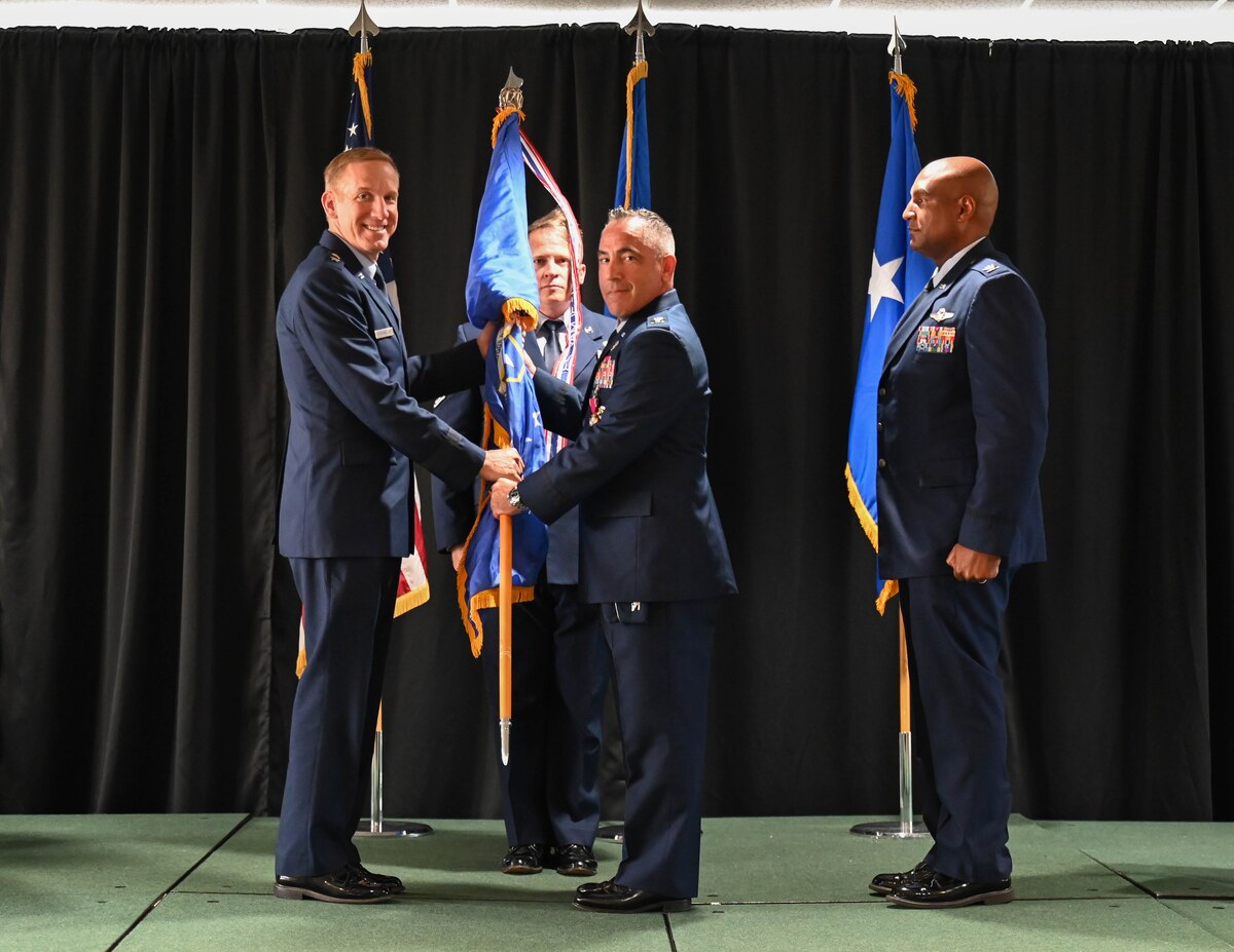 U.S. Air Force Maj. Gen. Case Cunningham, U.S. Air Force Warfare Center commander, left, accepts the guidon from U.S. Air Force Col. Josh Koslov, 350th Spectrum Warfare Wing outgoing commander, center, during the wing change of command ceremony at Eglin Air Force Base, Florida, July 9, 2024. Koslov oversaw the stand up of five units at the wing, including the historic 388th Electronic Warfare Squadron and 563d EWS, along with the initial detachments that are projected to become the future 950th Spectrum Warfare Group at Robins AFB, GA, focusing on the assessment of Air Force Electromagnetic Warfare capabilities to ensure the readiness of the Combat Air Force. (U.S. Air Force photo by Senior Airman Anna Smith)