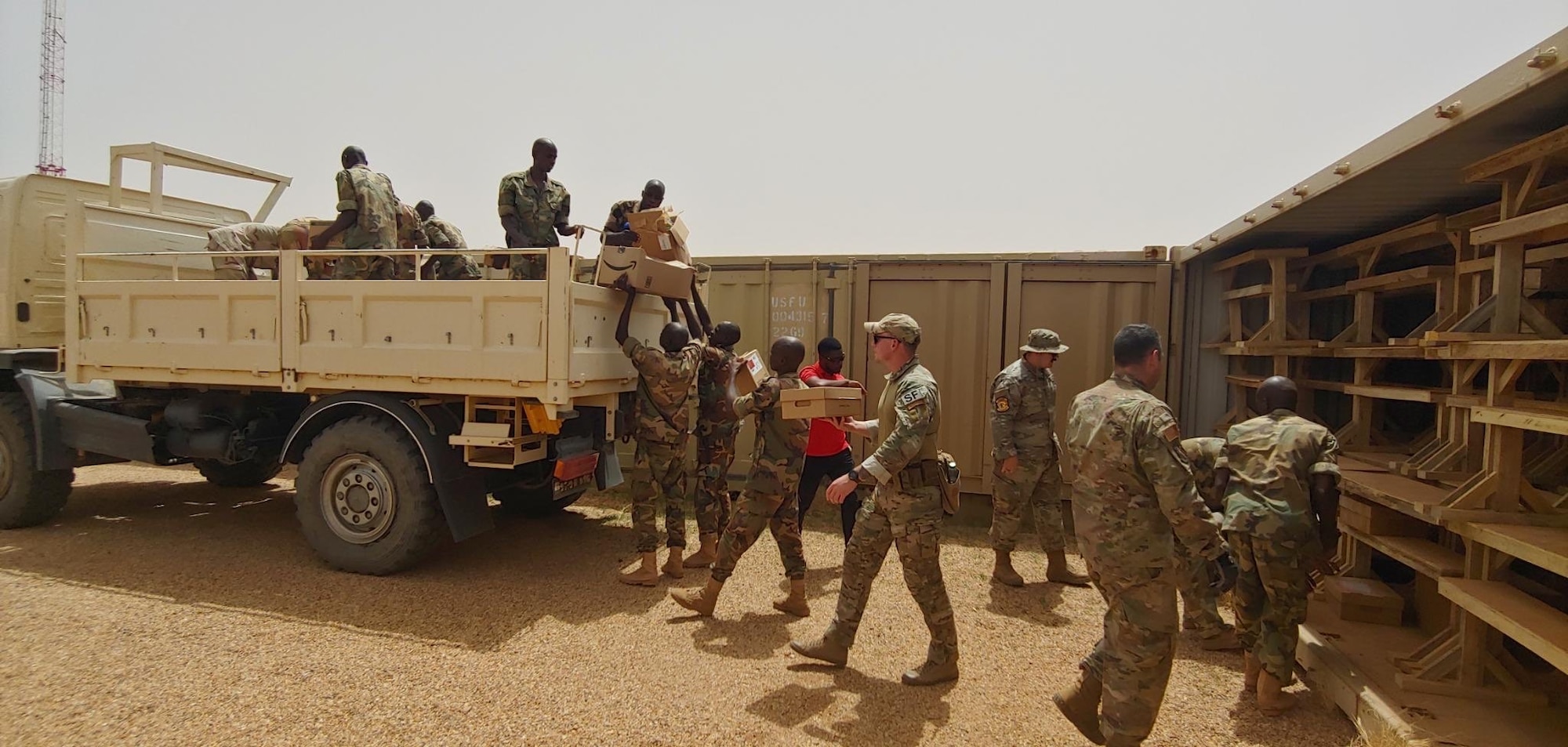 Military members wearing their uniform load desks onto a truck in a desert environment