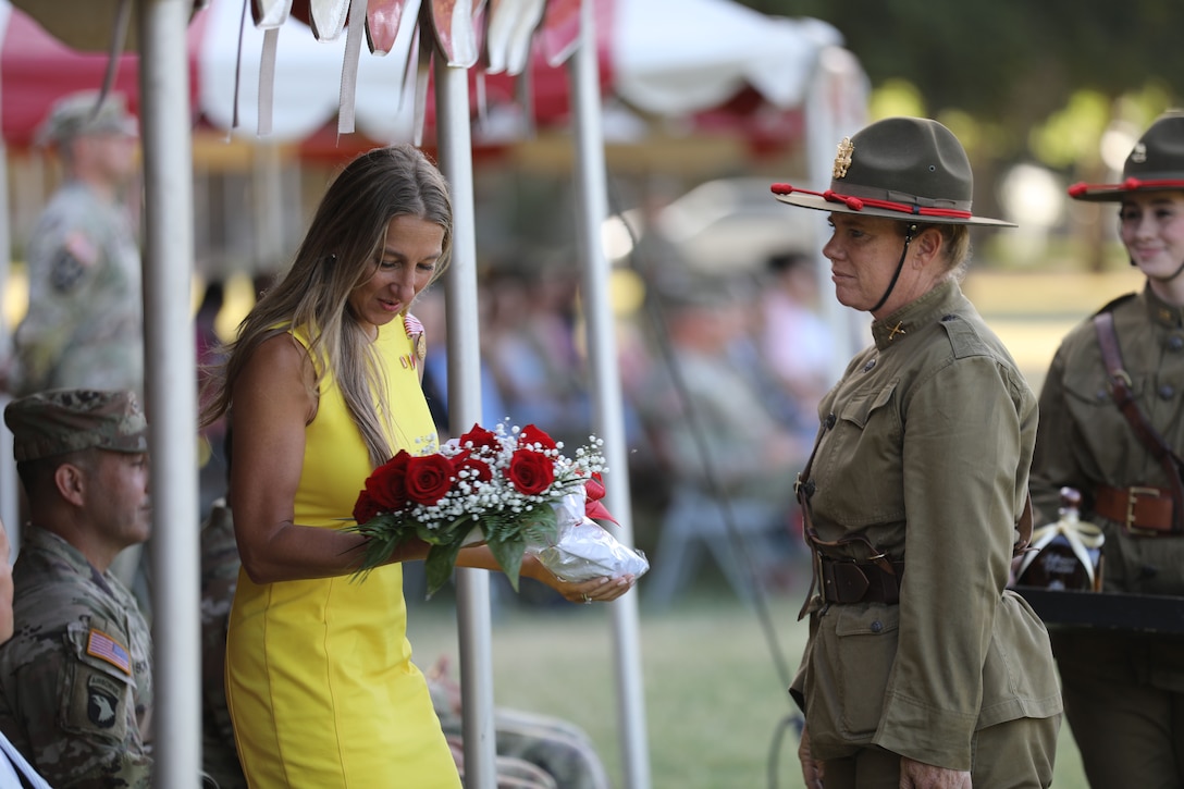 A woman in a yellow dress holds a bouquet of red roses as a soldier looks on.