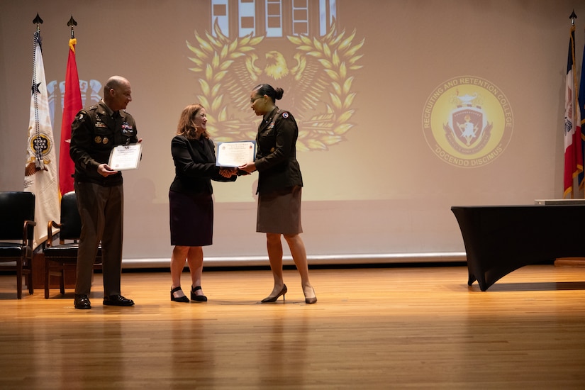women wearing U.S. Army uniform accepts a certificate from a women and man.