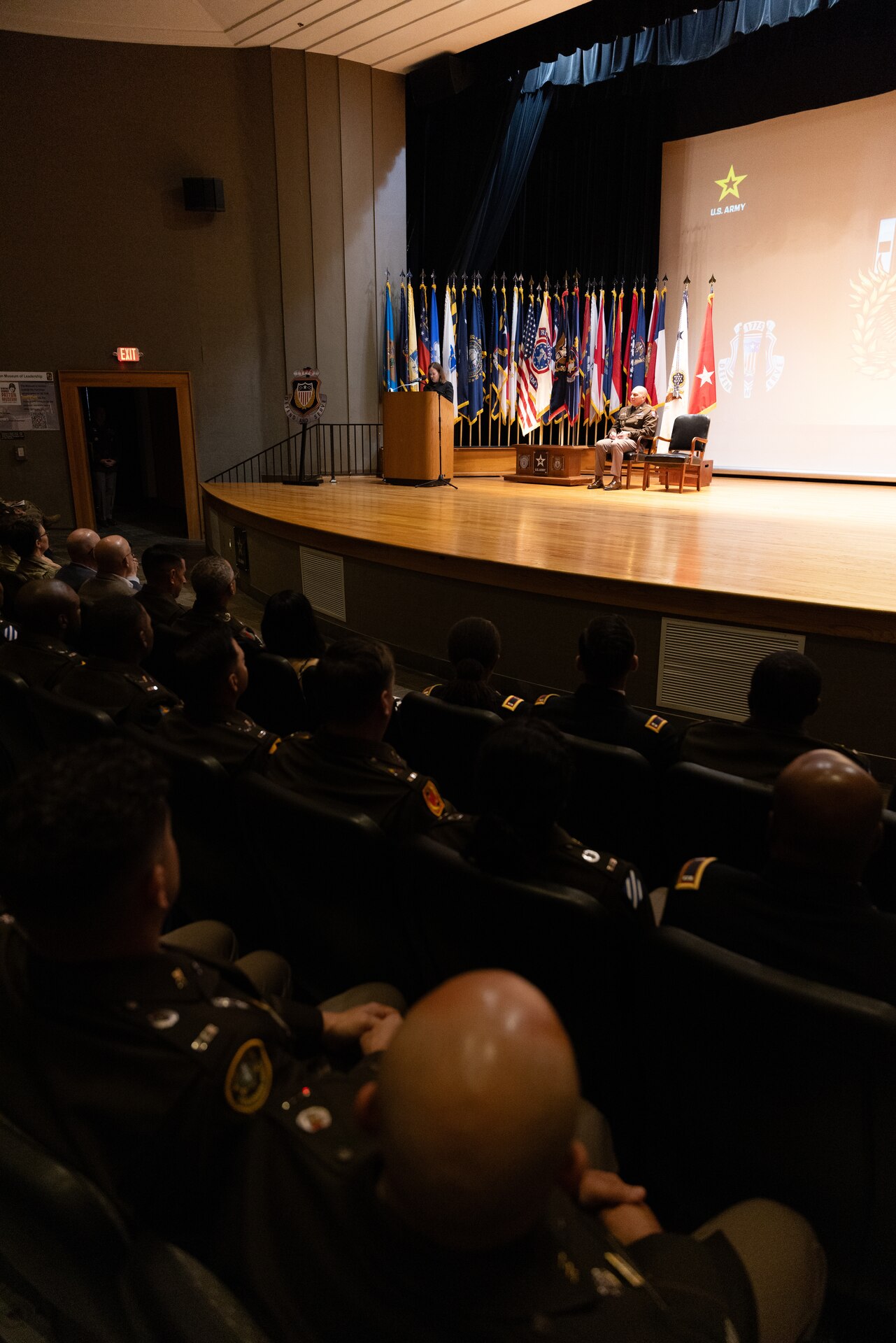 man and women speaking on stage with audience members seated listening.