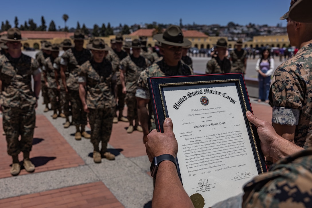 U.S. Marine Corps 1st Sgt. Julio Aguayo, a company first sergeant with Support Battalion, Recruit Training Regiment, reads the meritorious promotion warrant for Staff Sgt. Jose Salcedo, a chief drill instructor with Kilo Company, 3rd Recruit Training Battalion, at Marine Corps Recruit Depot San Diego, California, July 2, 2024. Salcedo was meritoriously promoted to the rank of staff sergeant for his hard work, dedication to duty, and excelling beyond his peers.  Meritorious promotions are based on outstanding performance and the Marine's ability to take on more responsibility and authority. Nominees must also demonstrate leadership skills and be able to fulfill the duties of the next higher grade. (U.S. Marine Corps photo by Sgt. Jesse K. Carter-Powell)