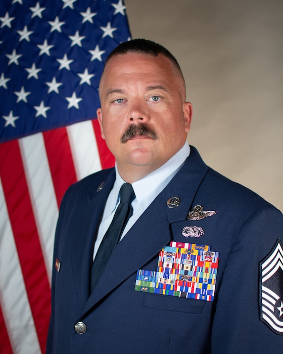 Service member poses for official portrait in front of the US flag wearing their service dress blues.