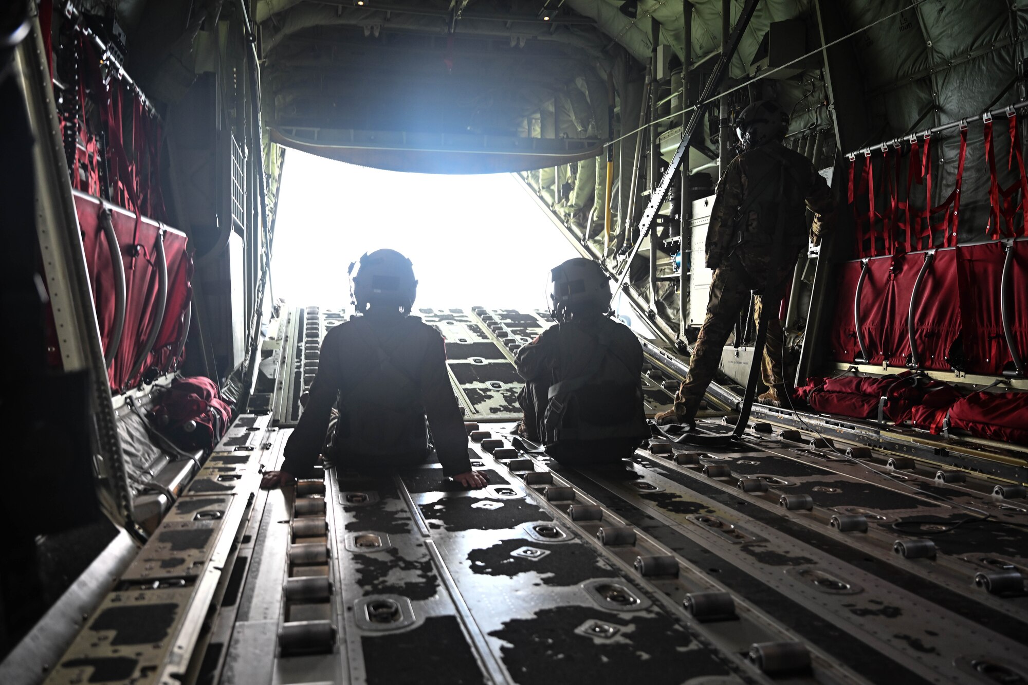 People in uniform watch as a ramp door opens on a military aircraft.