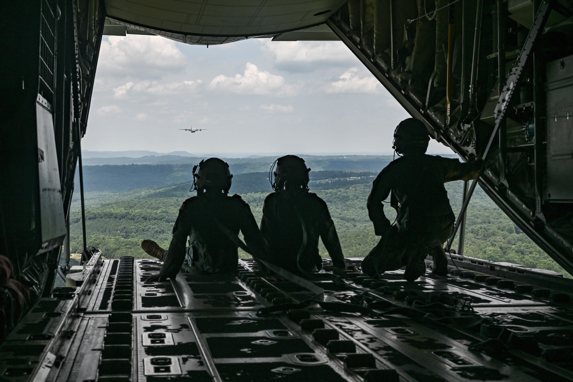 People in uniform sit on a ramp door of a military aircraft.