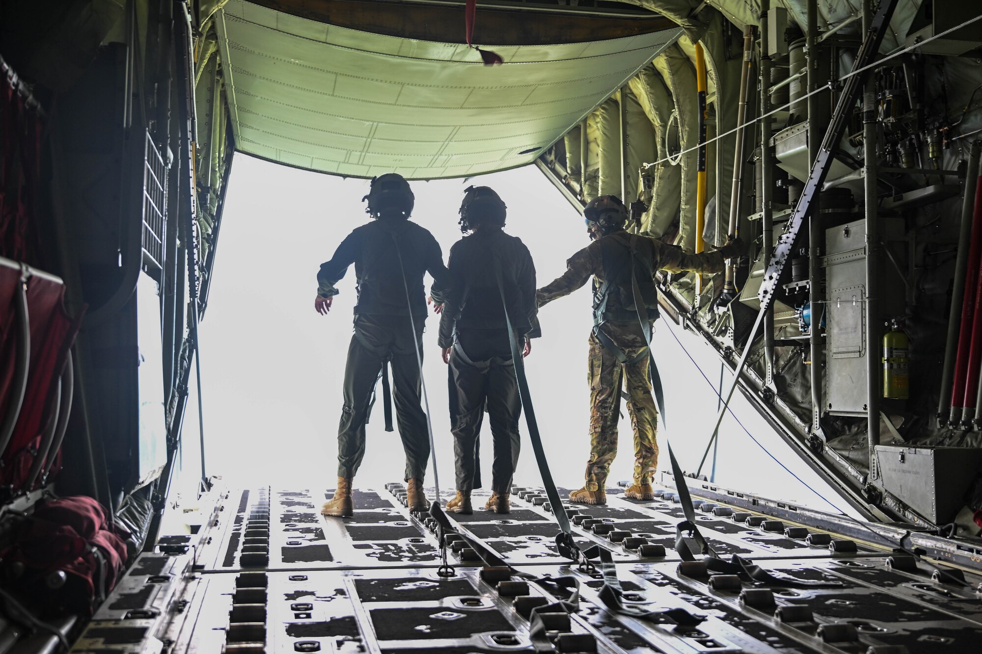 Three people in uniform walk on the ramp door of a military aircraft.