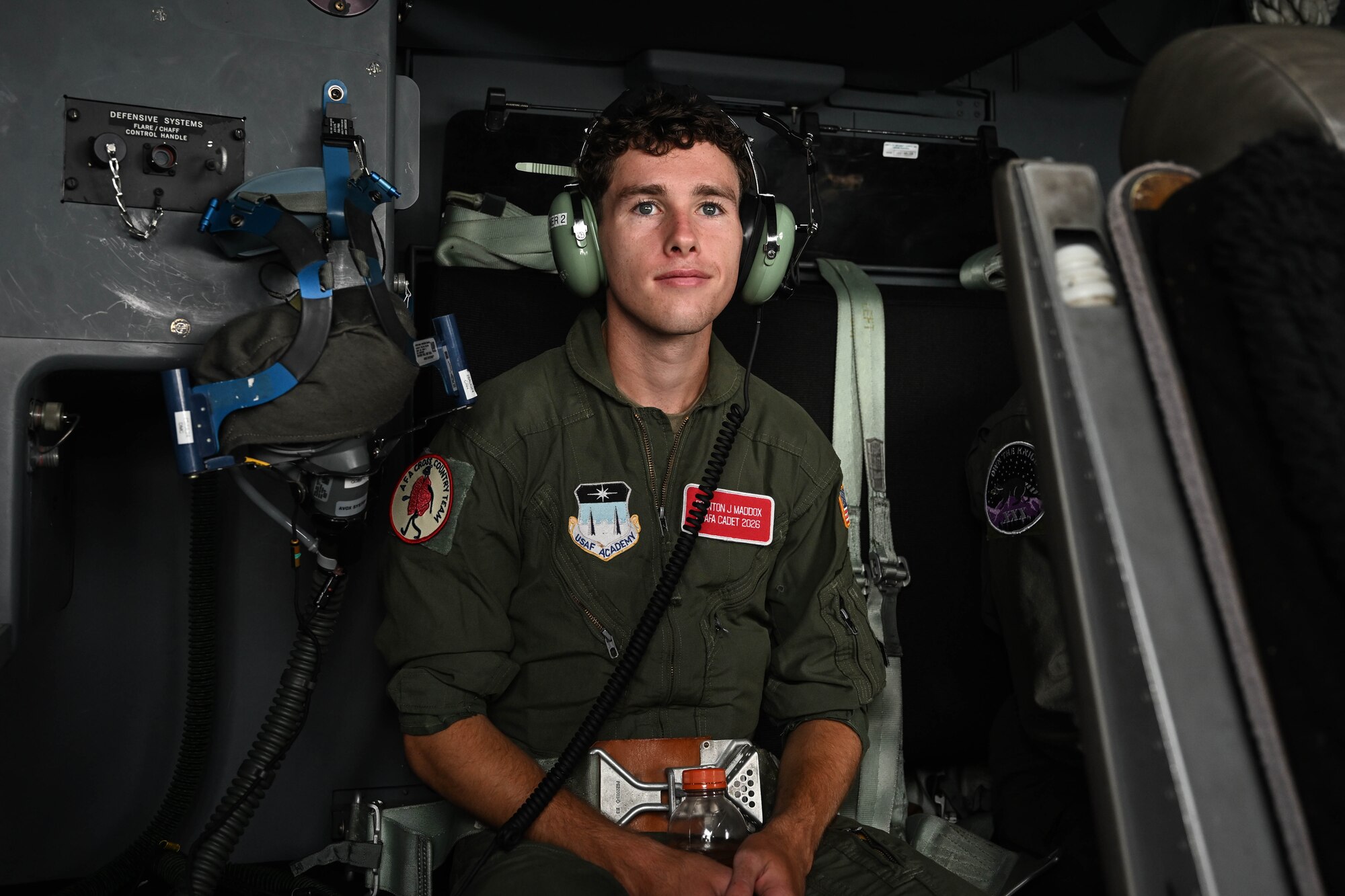 A man in uniform sits and smirks sitting down on a military aircraft.