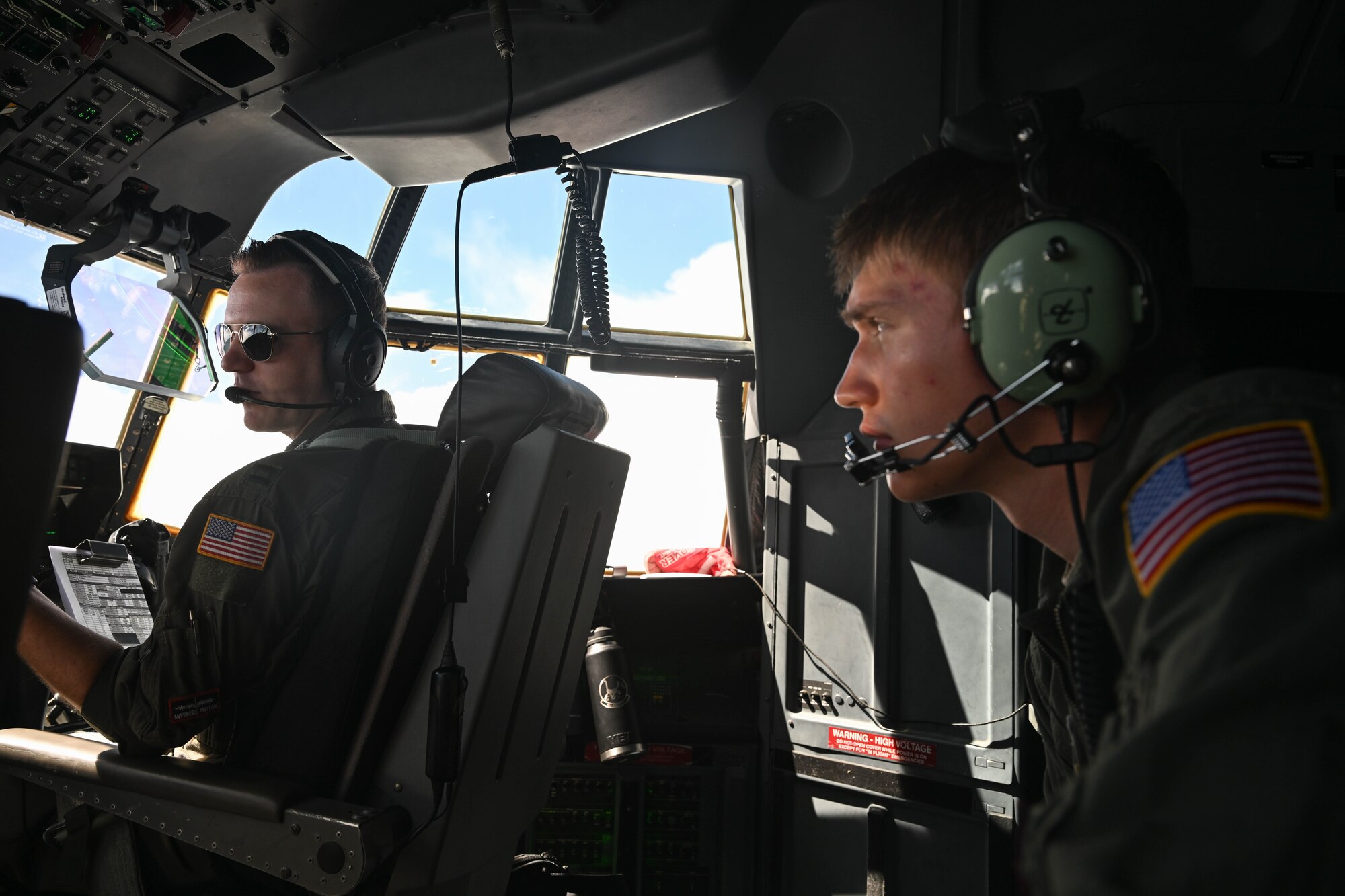 A man in uniform talks to a pilot during flight in a military aircraft.