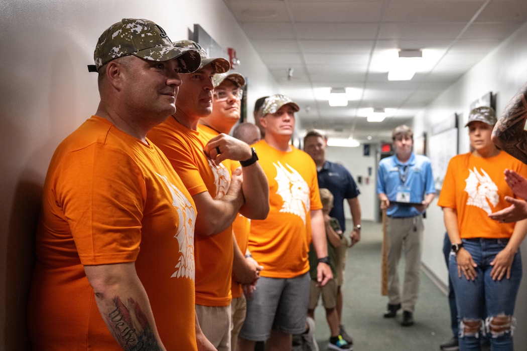 A group of individuals wearing orange shirts are briefed in a hallway.