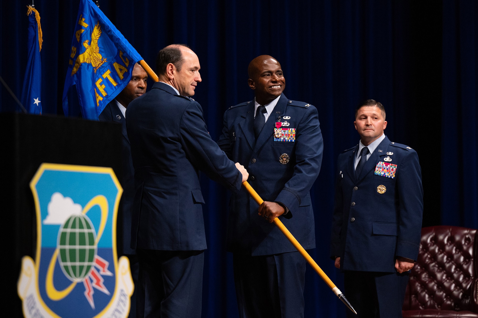 Col. James A. Finlayson, outgoing commander of the Air Force Technical Applications Center, passes the unit guidon to Lt. Gen. Kevin B. Kennedy, 16th Air Force commander and presiding officer, during a Change of Command ceremony at Patrick Space Force Base, Fla., July 11, 2024.  Also pictured are inbound AFTAC commander Col. Creighton A. Mullins and Chief Master Sgt. Jerome Wright, AFTAC’s command chief.  (U.S. Air Force photo by Amanda Inman)