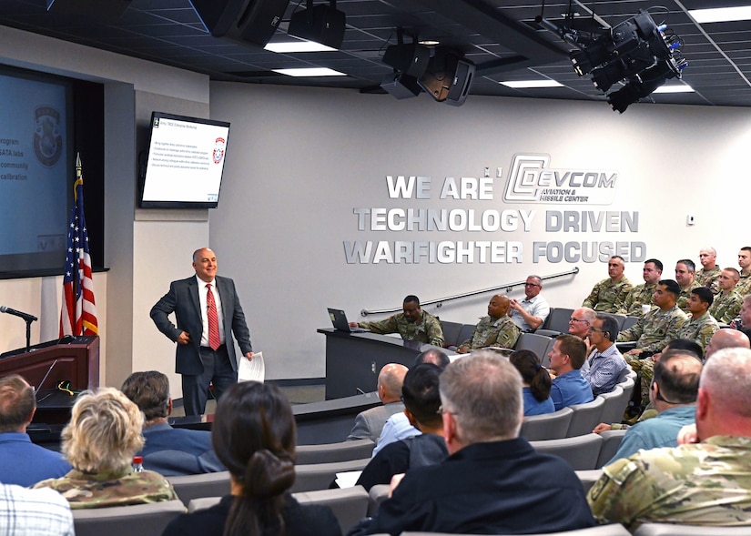 Man on stage talking to Soldiers.