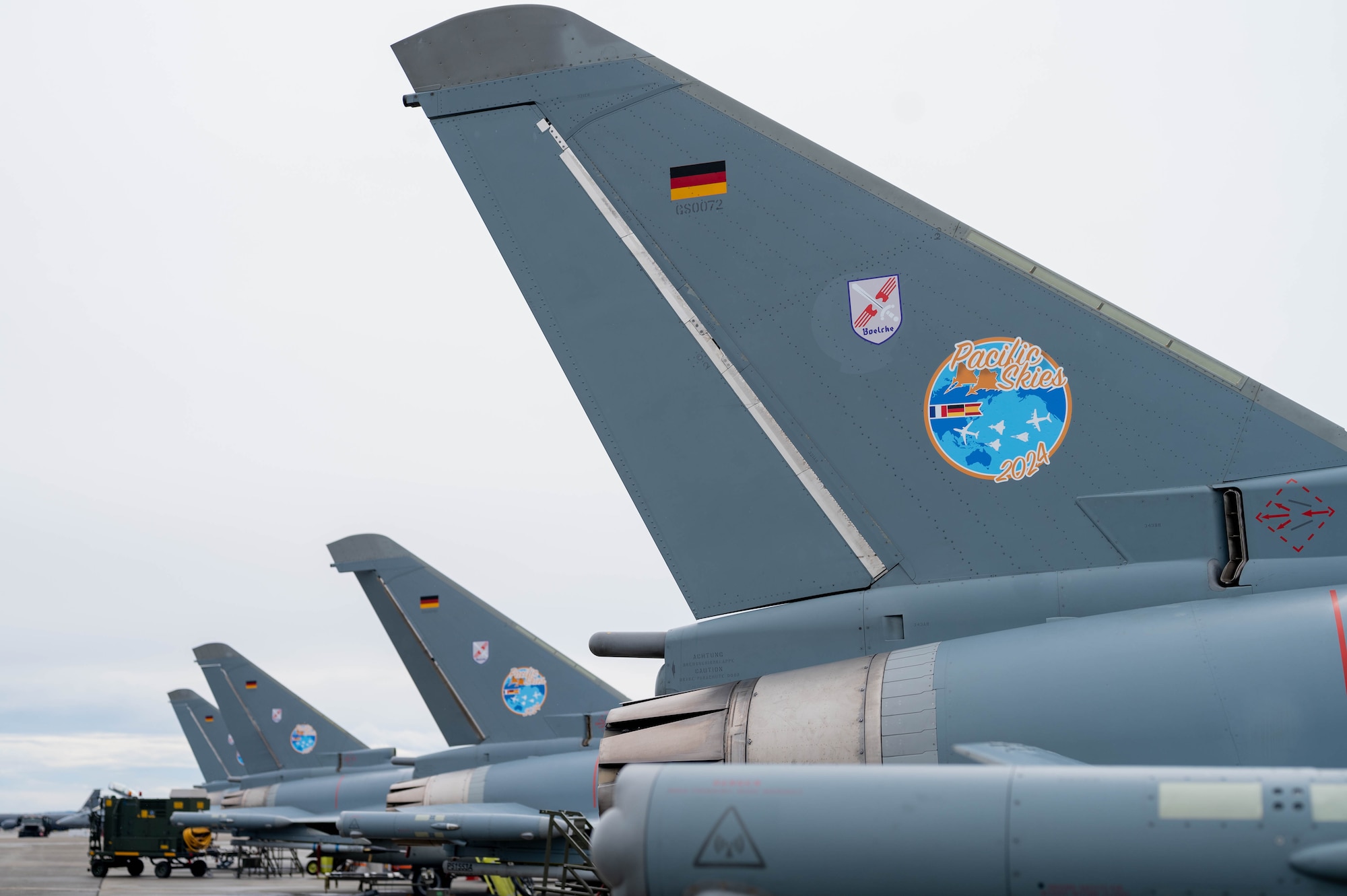 Tails from the German Air Force Eurofighters sit lined up in a diagonal pattern on the flightline.