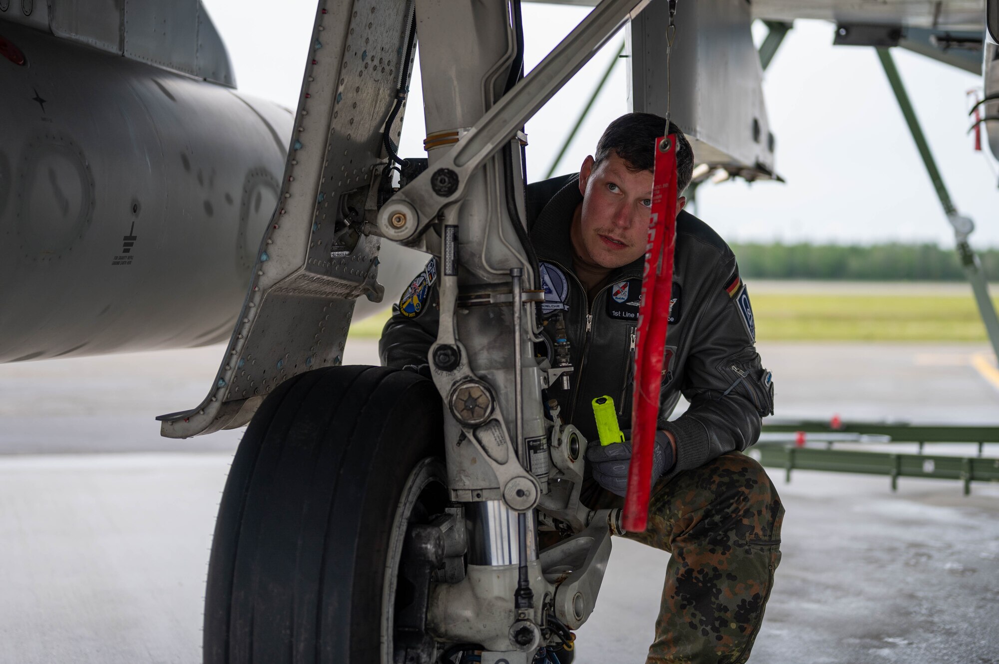 A maintainer assigned to the German Air Force squats next to an aircraft tire to conduct an inspection.