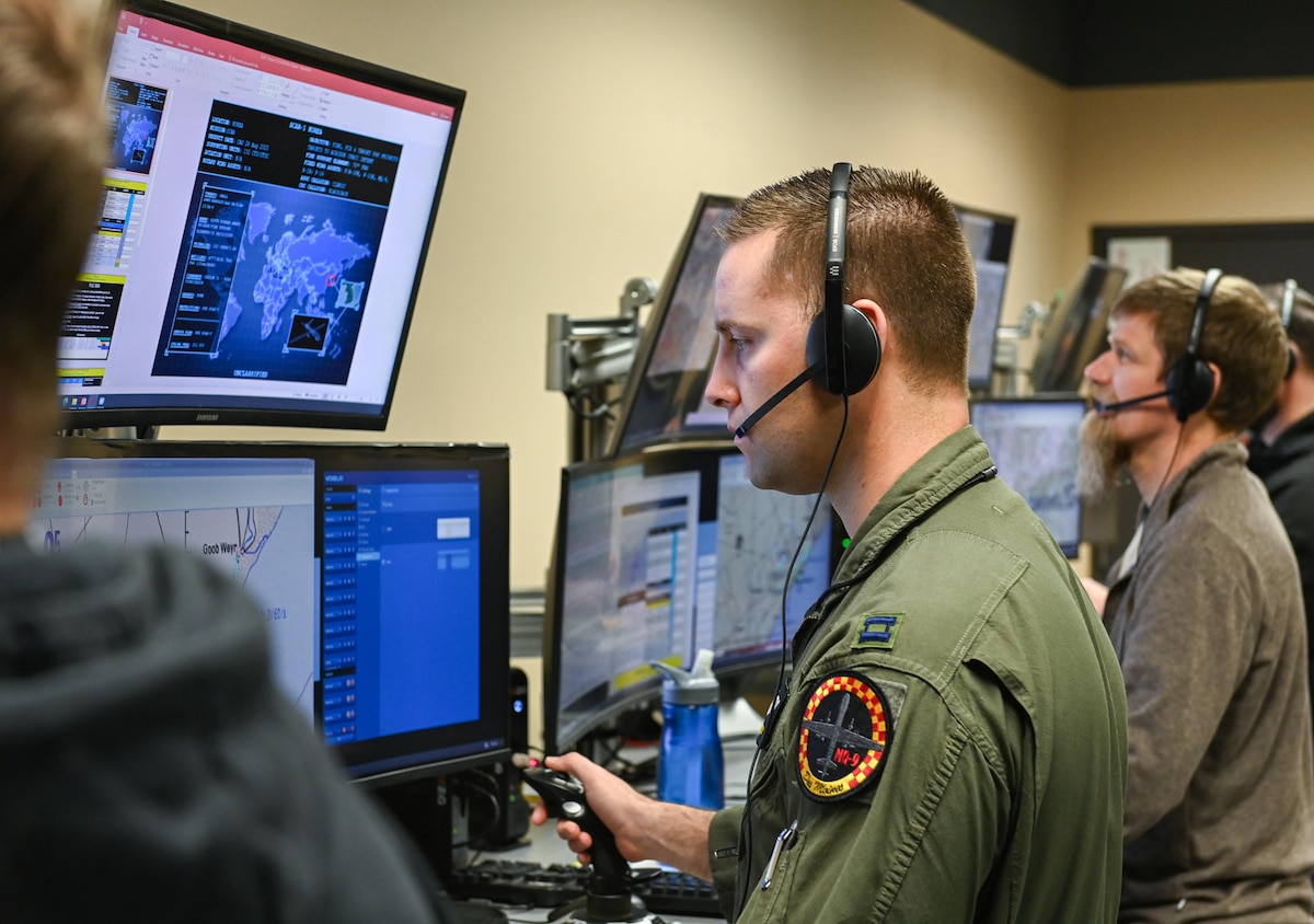 A pilot in green flight suit stands by a computer using a joystick during an exercise.