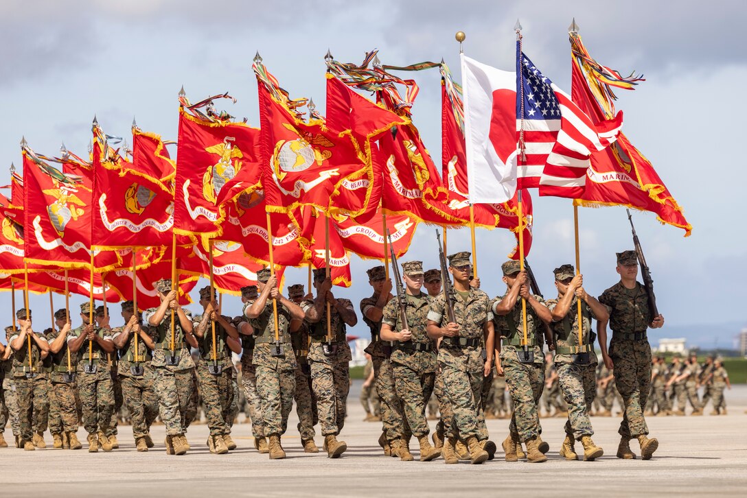 U.S. Marines with 1st Marine Aircraft Wing march with their unit colors during a change of command ceremony at Marine Corps Air Station Futenma, Okinawa, Japan, July 12, 2024. During the ceremony, Maj. Gen. Eric E. Austin relinquished command to Maj. Gen. Marcus B. Annibale. 1st MAW is the aviation combat element of III Marine Expeditionary Force. Its mission is to conduct air operations in support of the Fleet Marine Forces to include offensive air support, anti-air support, assault support, aerial reconnaissance, electronic warfare, and control of aircraft and missiles. (U.S. Marine Corps photo by Lance Cpl. Sav Ford)