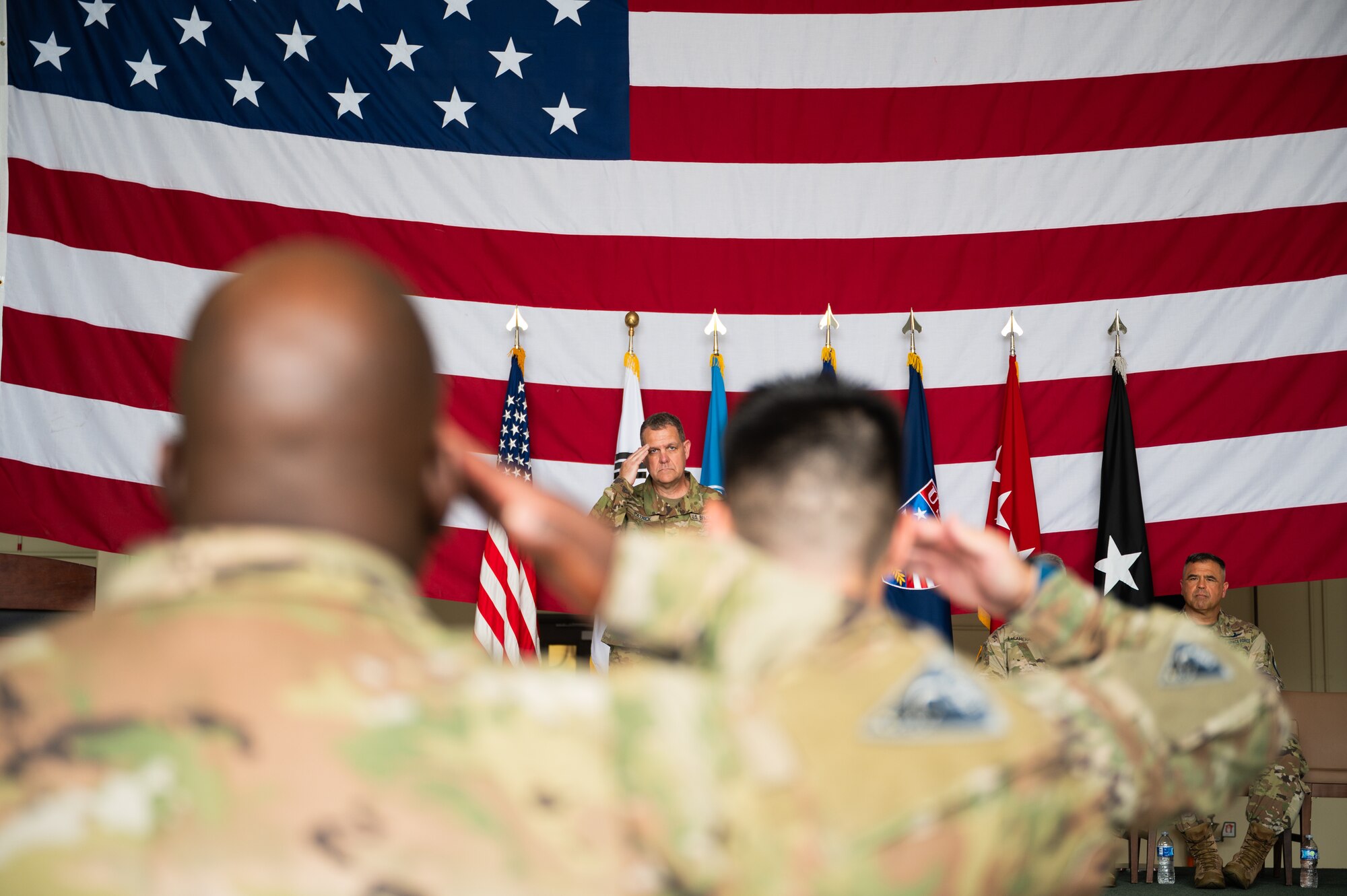 A Space Force Colonel is in focus facing the camera and salutes a formation of uniformed Space Force Guardians, who are also holding salutes and out of focus.