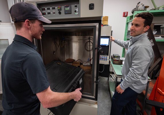 Naval Information Warfare Center (NIWC) Atlantic employees David Doyle (l), electrical engineer and Matt Paturzo (r), mechanical engineer, prepare and set up various equipment for environmental testing at NIWC Atlantic’s Environmental Test and Evaluation lab. The team prepares a television monitor for vibration susceptibility on a “shake table”. This test is designed to ensure that the equipment can withstand even the harshest conditions, providing unfailing support to Sailors and Marines when it is needed most.