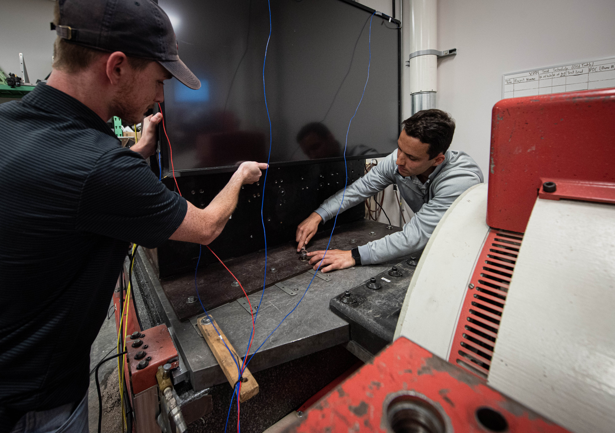 Naval Information Warfare Center (NIWC) Atlantic employees David Doyle (l), electrical engineer and Matt Paturzo (r), mechanical engineer, prepare and set up various equipment for environmental testing at NIWC Atlantic’s Environmental Test and Evaluation lab. The team prepares a television monitor for vibration susceptibility on a “shake table”. This test is designed to ensure that the equipment can withstand even the harshest conditions, providing unfailing support to Sailors and Marines when it is needed most.