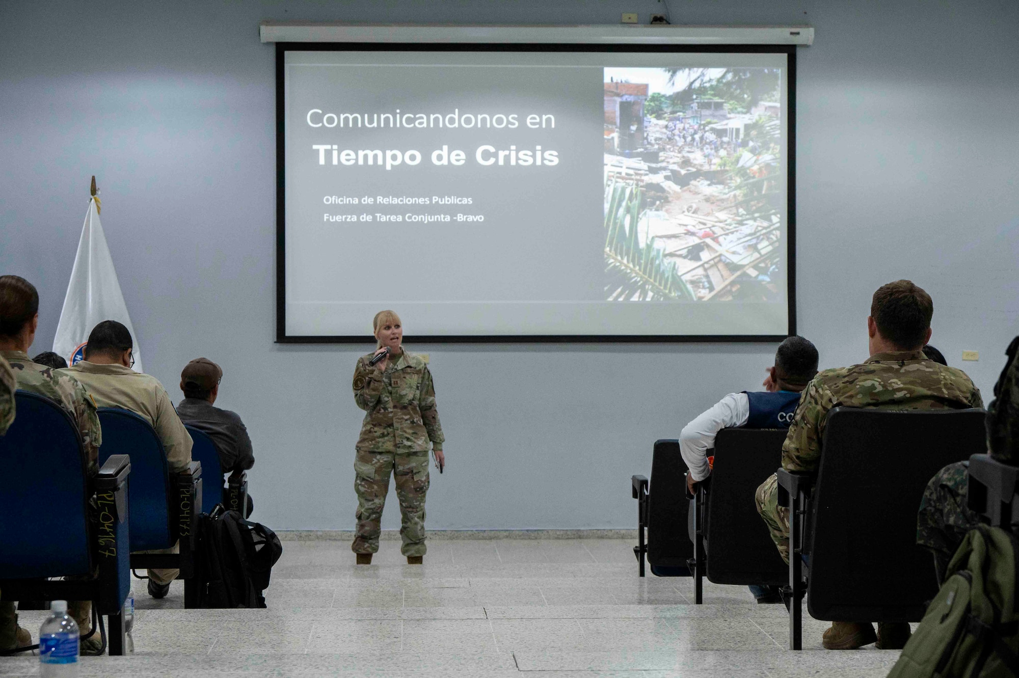 A photo of a military member speaking in a microphone during a presentation.