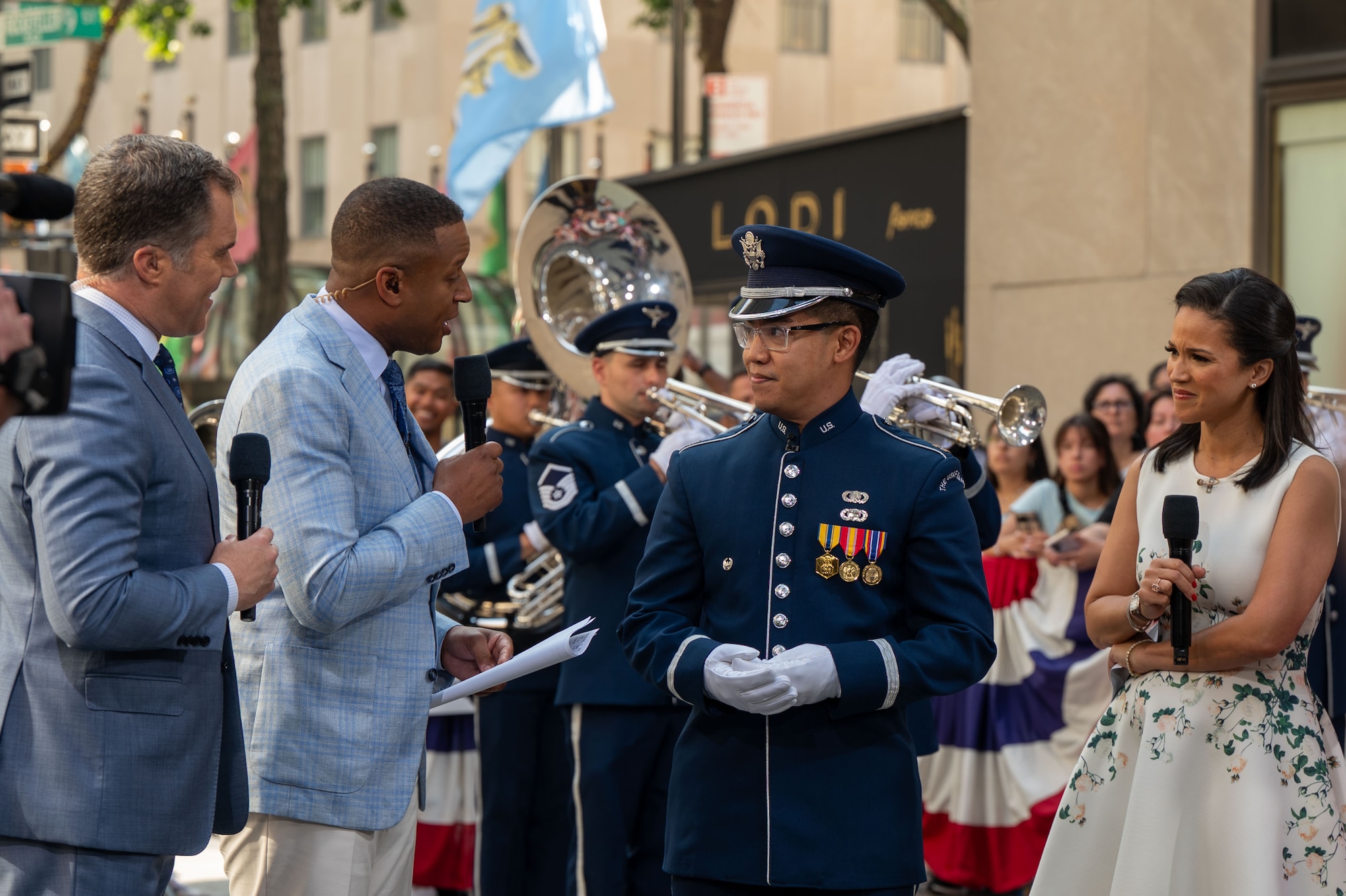 reporters interview military officer with musicians and crowd in back