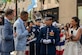 reporters interview military officer with musicians and crowd in back