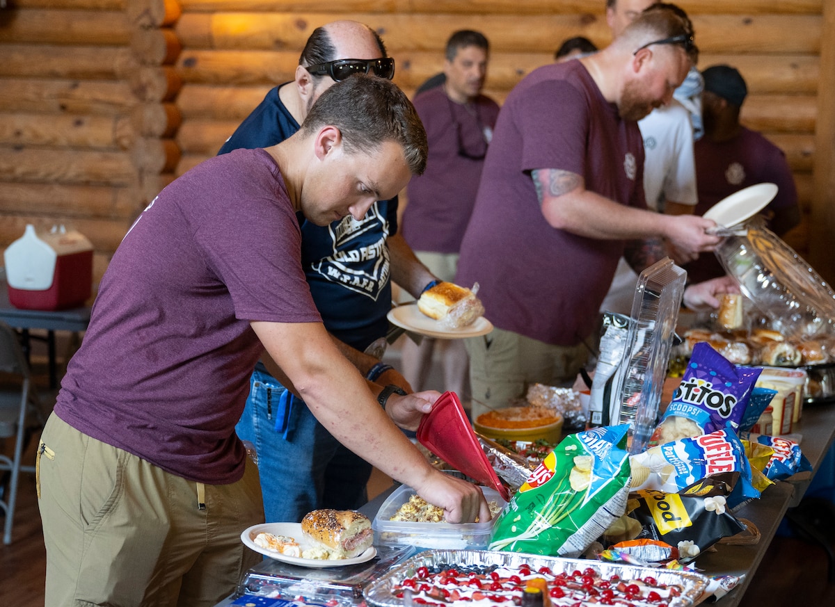 A line of people in maroon tee shirts make their way down a table loaded with food.