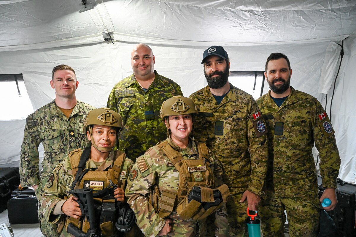 Tech Sgt. Marisa Fernandez, 433rd Contingency Response Flight specialist and Staff Sgt. Ana Quintanilla, 433rd CRF specialist pose for a photo with Lt. Commander Nathan Cooley, Canadian Liaison for the Office of Naval Intelligence, Capt. Alan Morgan, Royal Canadian Air Force 2 Wing plans officer, and other RCAF members after discussion on how CR teams establish communications, processes aircraft, and manages an airfield at the Contingency Location Operations Rehearsal (CLOR 24) in Alpena, Michigan June 24, 2024.