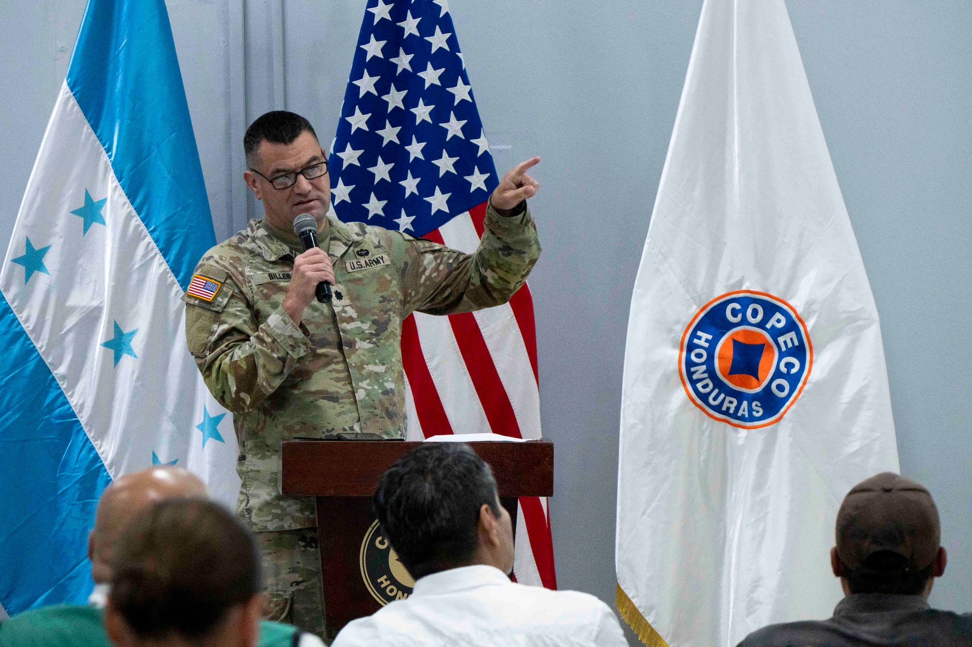 A photo of a military member speaking at a podium with a microphone.