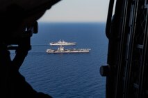Two military ships are seen from above steaming in formation across the water.